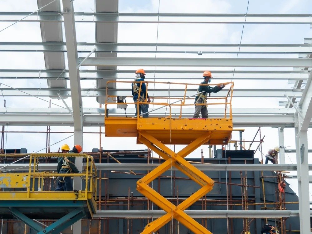 Construction workers on a lift, installing materials on a building under construction against a clear blue sky.