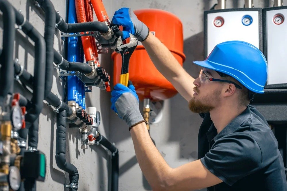A man in a hard hat and safety glasses is working on a water heater, demonstrating safety and professionalism in his work.